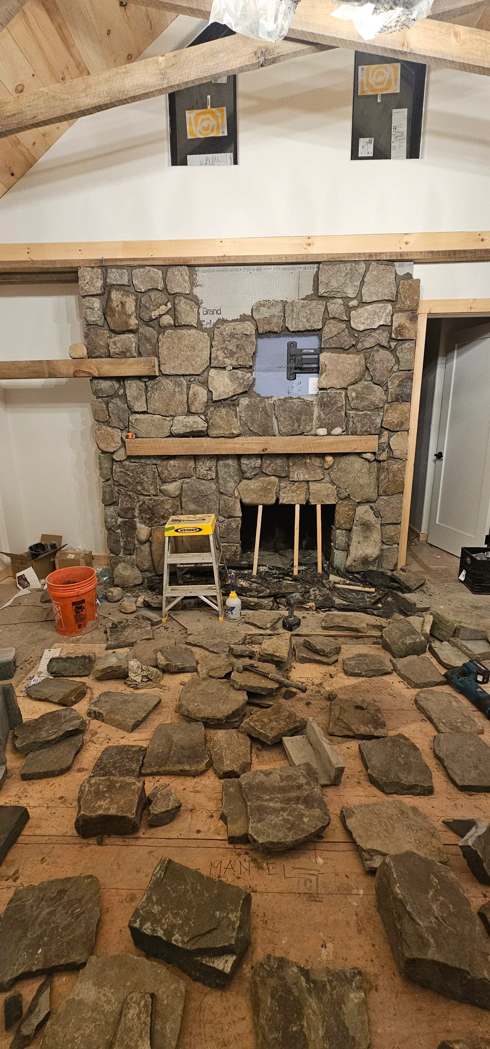 Stacked stone fireplace with natural stone veneer, exposed wood beams, and firebox opening under construction