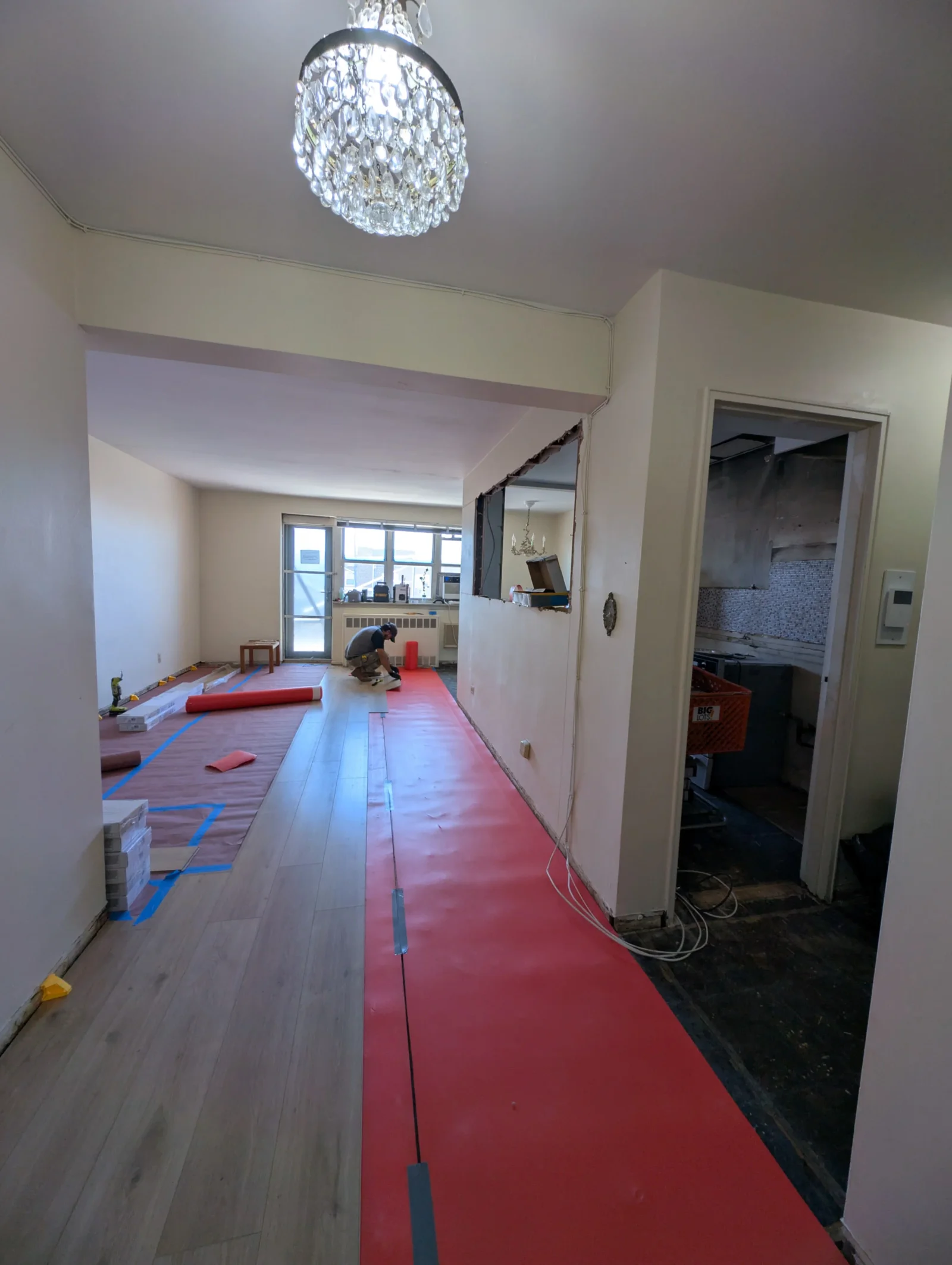 Hardwood floor installation in progress with protective red coverings and blue tape masking in residential interior