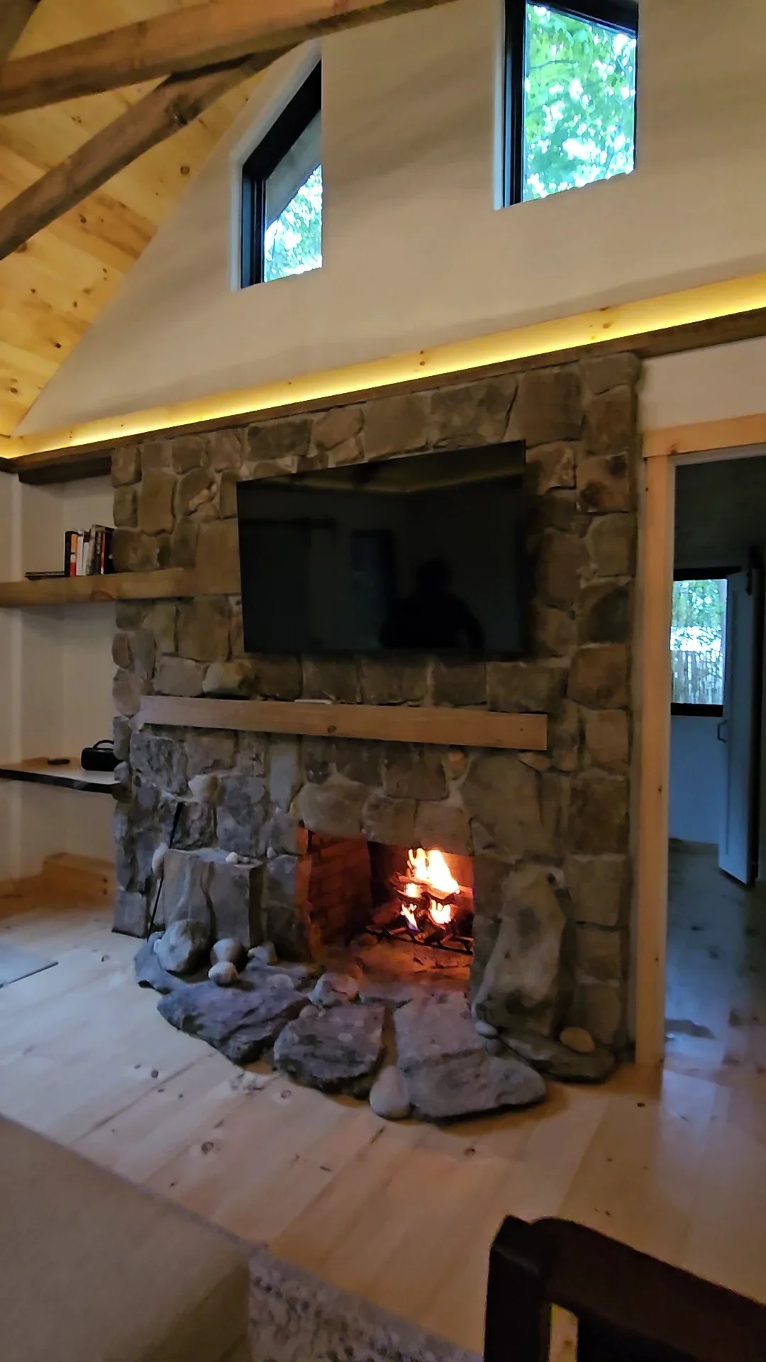 Stone fireplace with TV mount, active fire, recessed lighting, and exposed timber beams