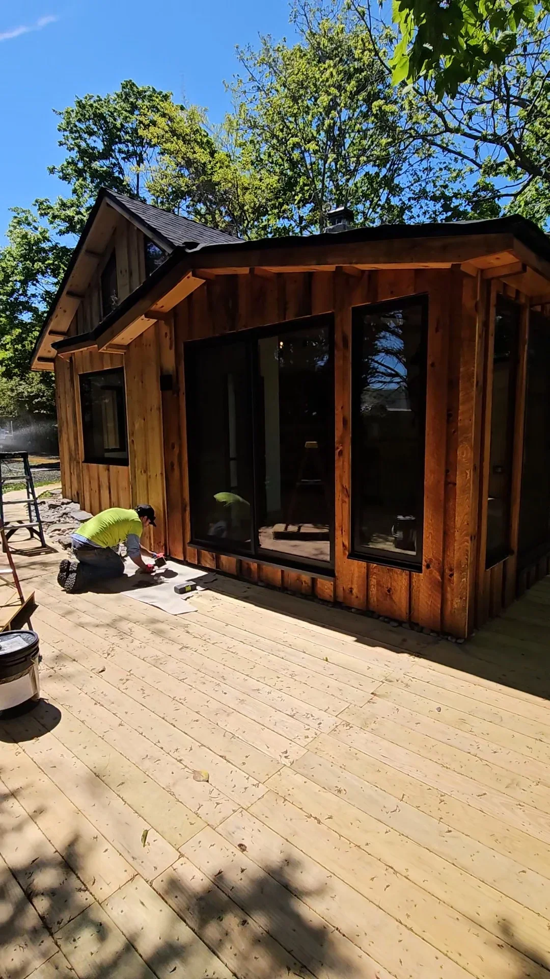 Cedar cabin addition with black windows and new pressure-treated deck during staining