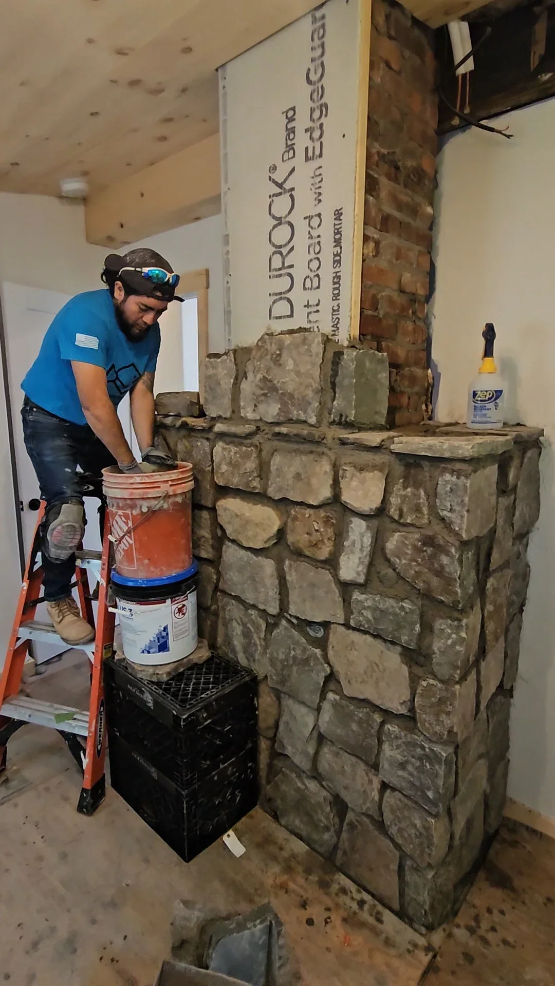Craftsman applying mortar to stacked stone fireplace with tan and gray blocks