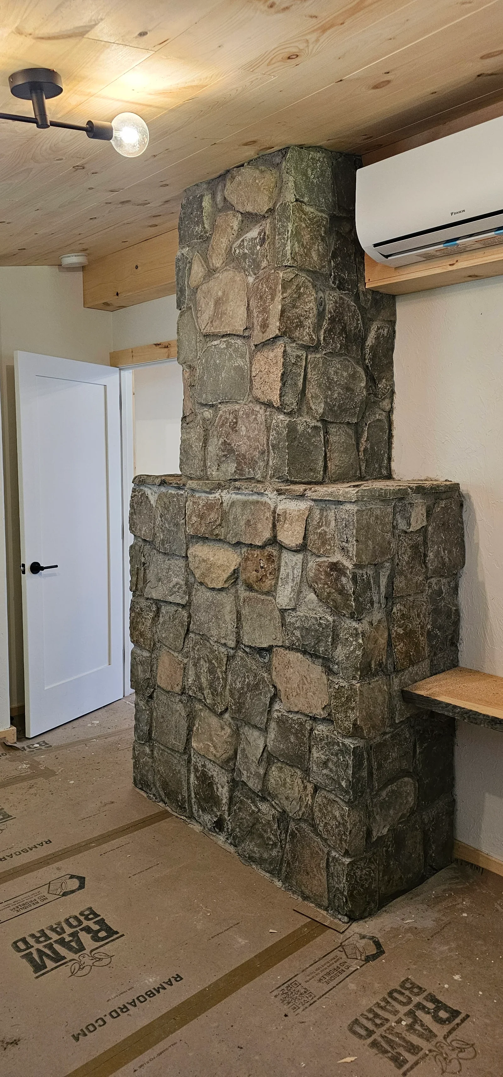 Stacked fieldstone chimney with varied tan and gray stones, floor-to-ceiling installation in interior space
